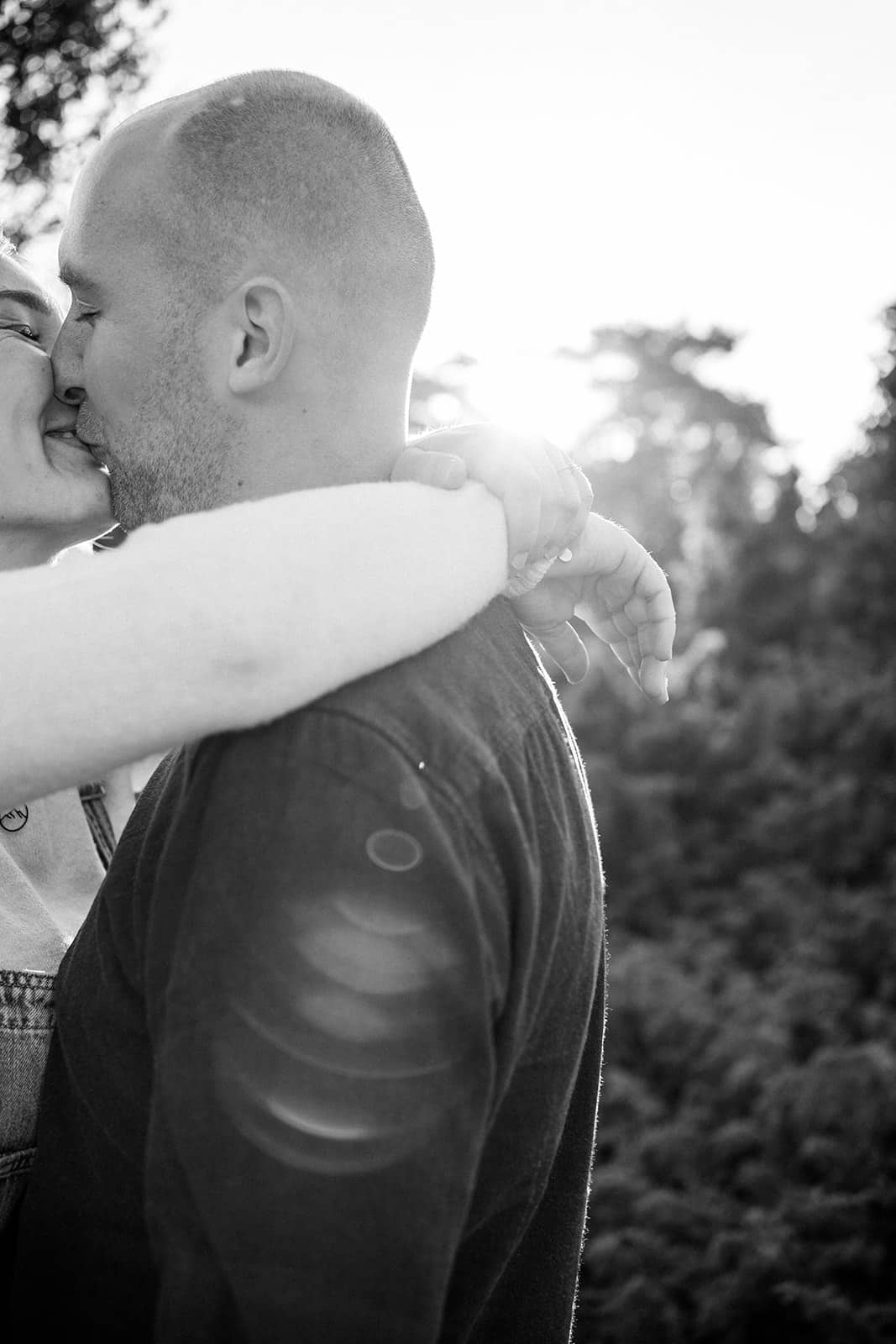 Verliebtes Paar bei einem Paarshooting in Ahaus, inniger Kuss in der Natur mit Sonnenflare, Schwarz-Weiß.