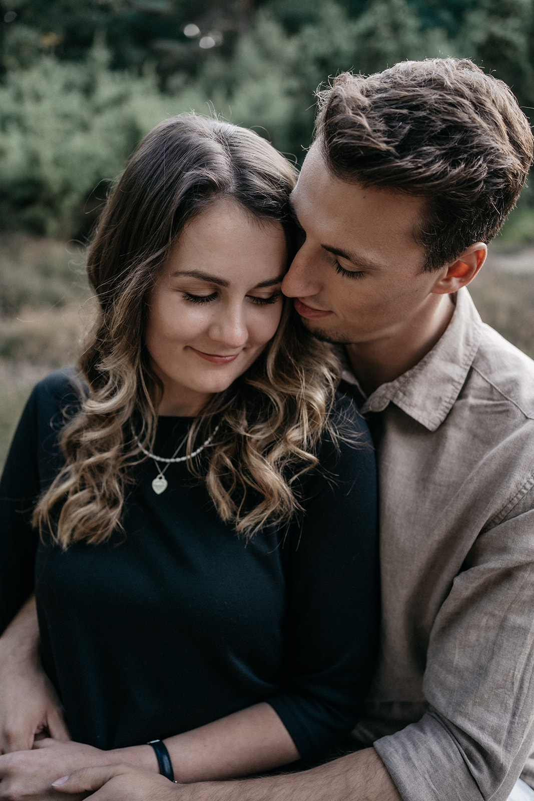 Verliebtes Paar bei einem Paarshooting in Ahaus, er umarmt sie sanft von hinten im Grünen.