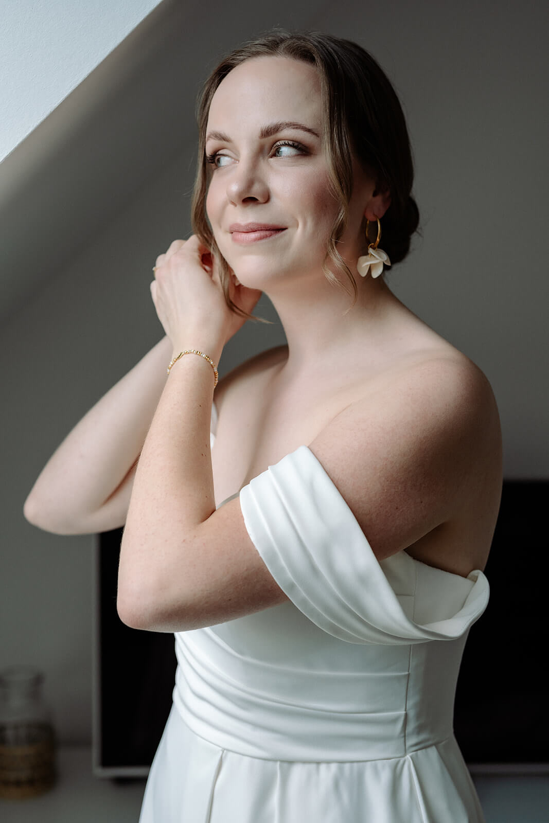 Strahlende Braut steckt sich Ohrring beim getting ready an – Hochzeitsfotografie Ahaus.