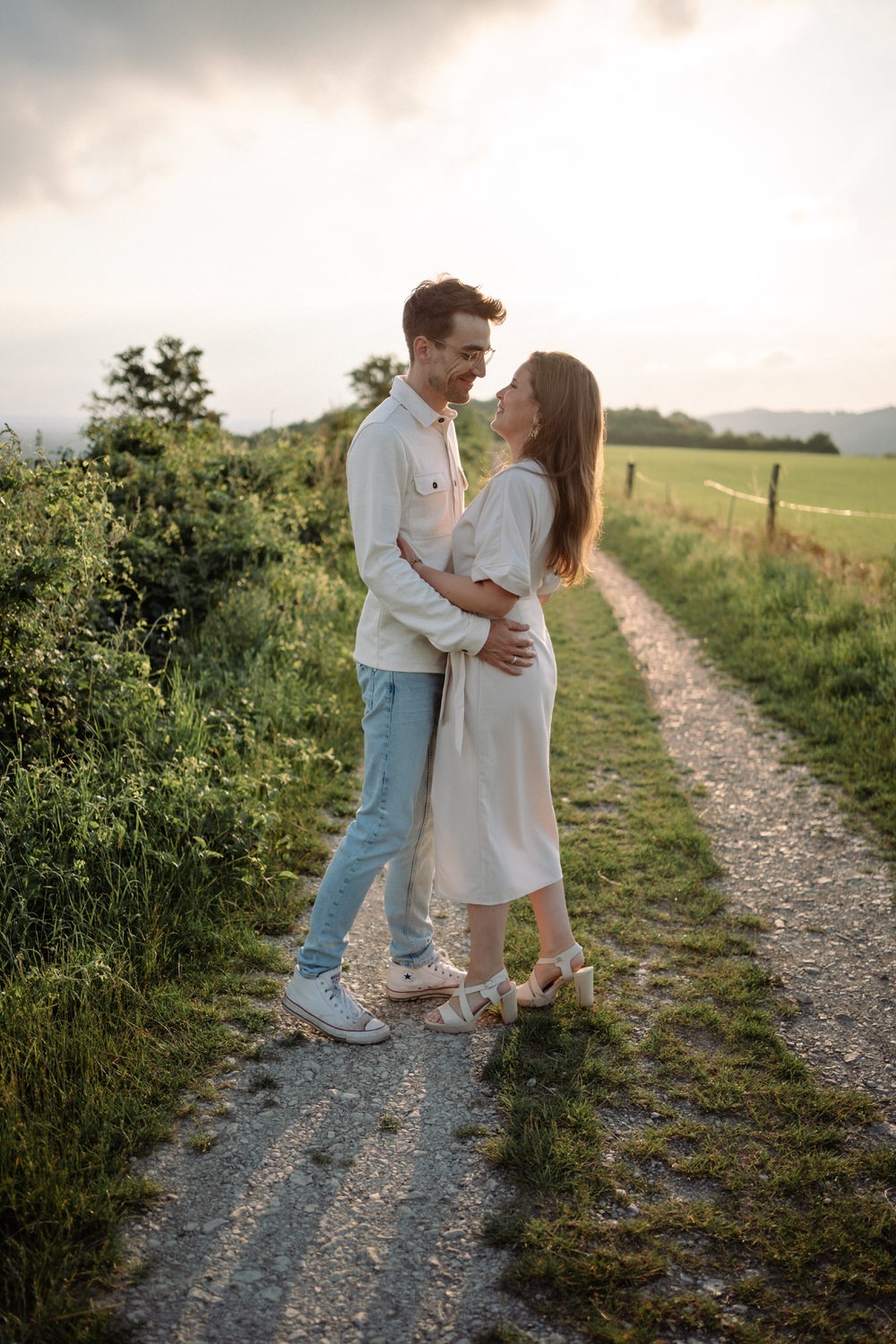 Lächelndes Paar beim Paarshooting in Ahaus, inniger Moment auf einem Feldweg bei Sonnenuntergang.