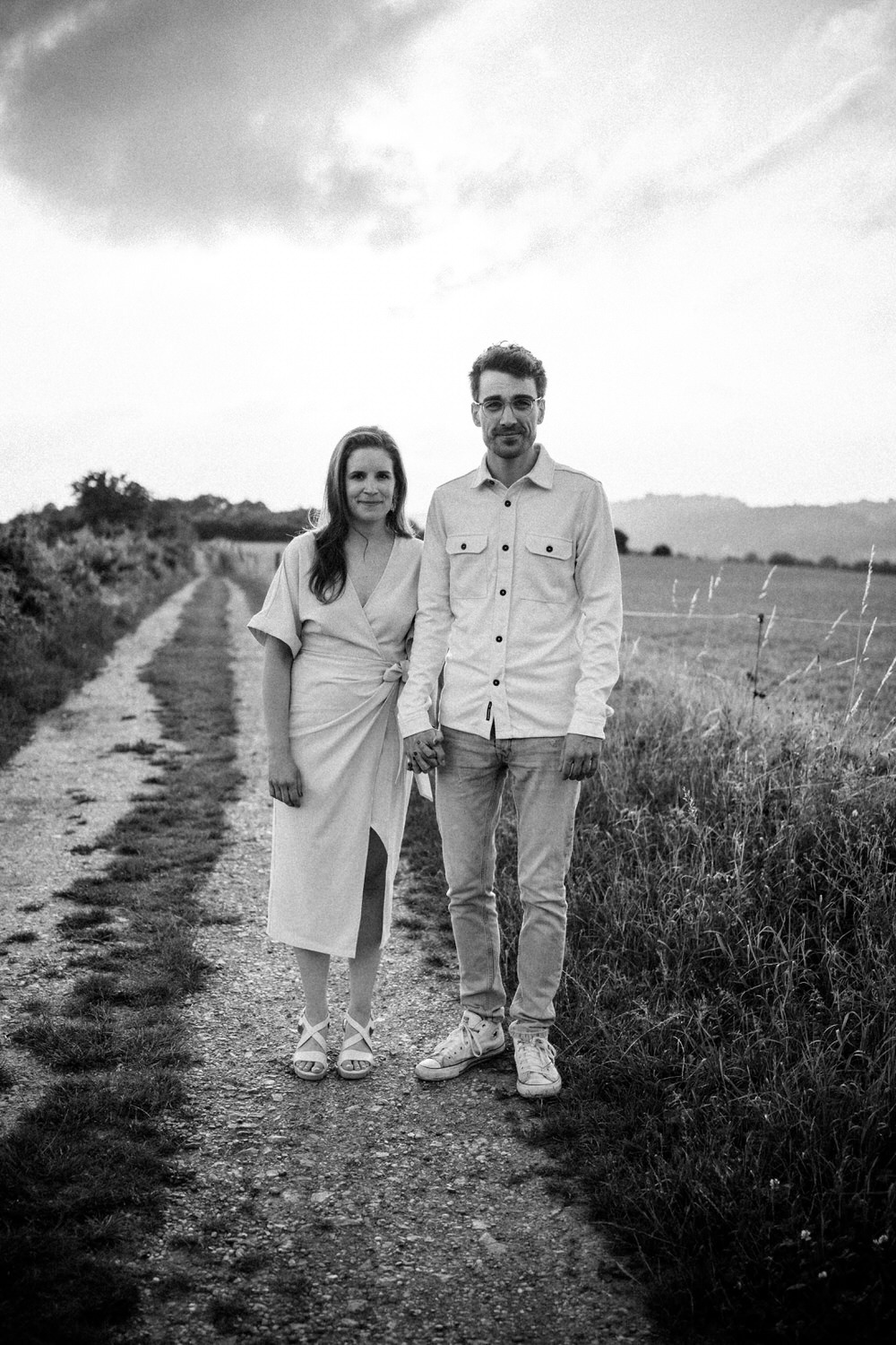Paar beim Paarshooting in Ahaus, hält sich an den Händen auf einem Feldweg, stilvolle Schwarz-Weiß-Aufnahme.