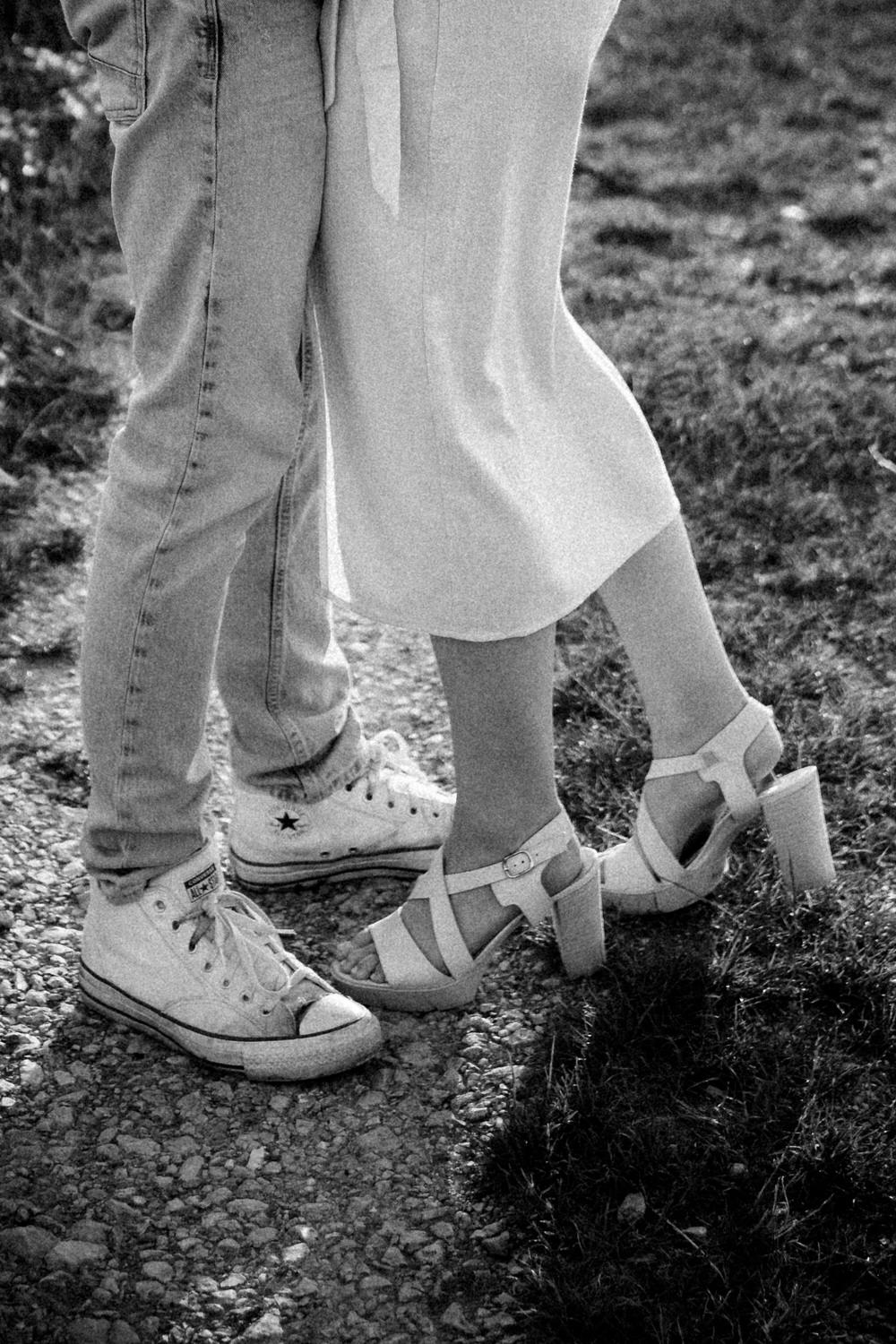 Detailaufnahme eines Paares beim Paarshooting in Ahaus, ihre Füße in High Heels und seine in Sneakers festgehalten in schwarz weiß.