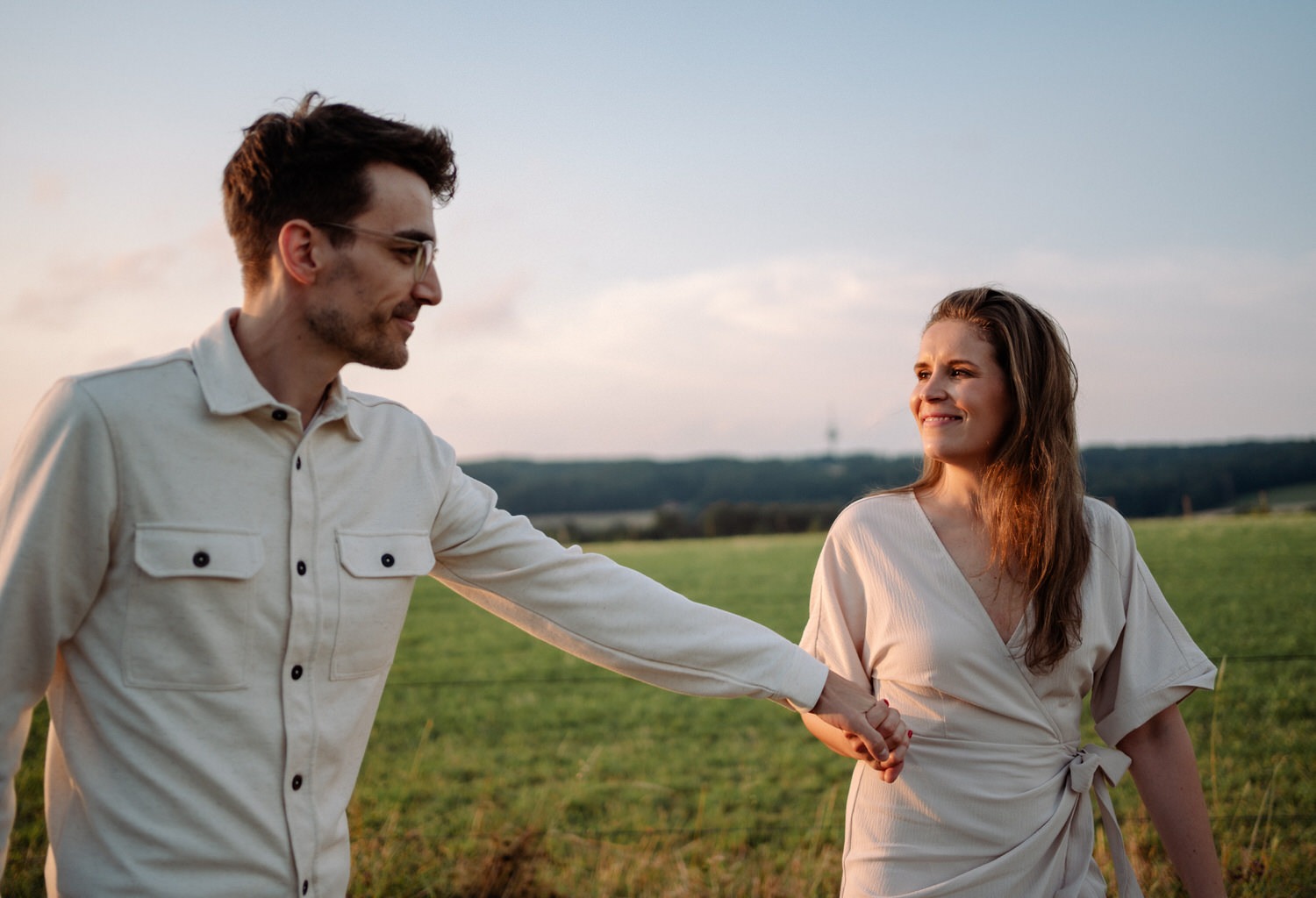 Verliebtes Paar beim Paarshooting in Ahaus, hält sich lächelnd an den Händen in der Abendsonne.