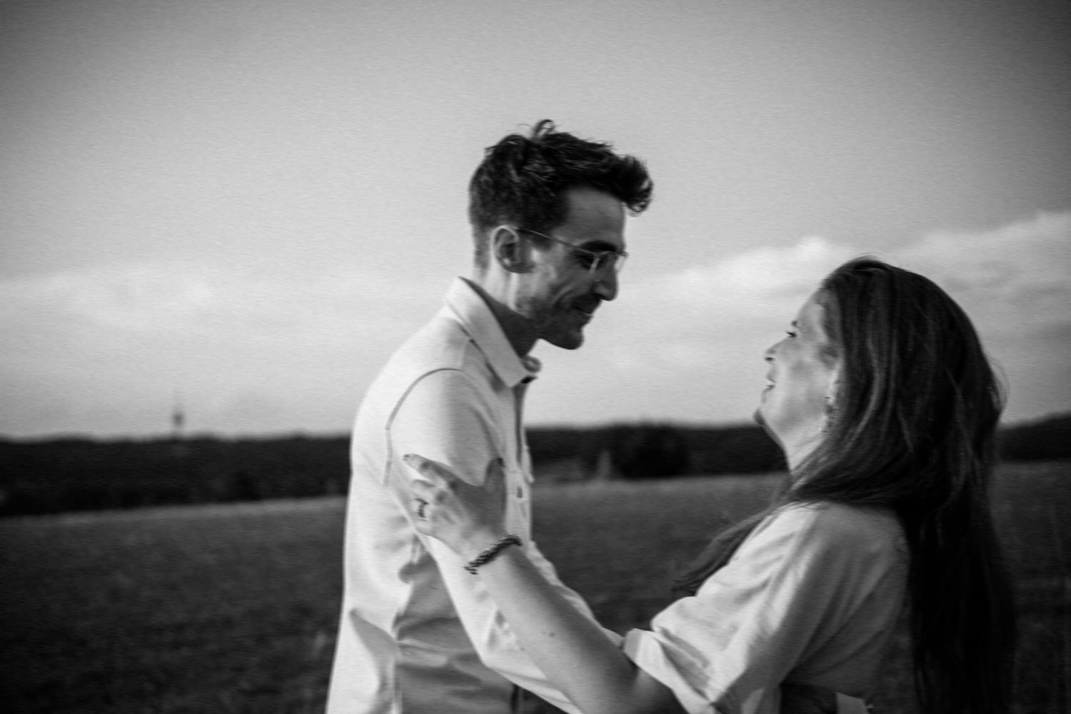 Lachendes Paar beim Paarshooting in Ahaus, romantischer Moment auf einem Feld, Schwarz-Weiß-Aufnahme.