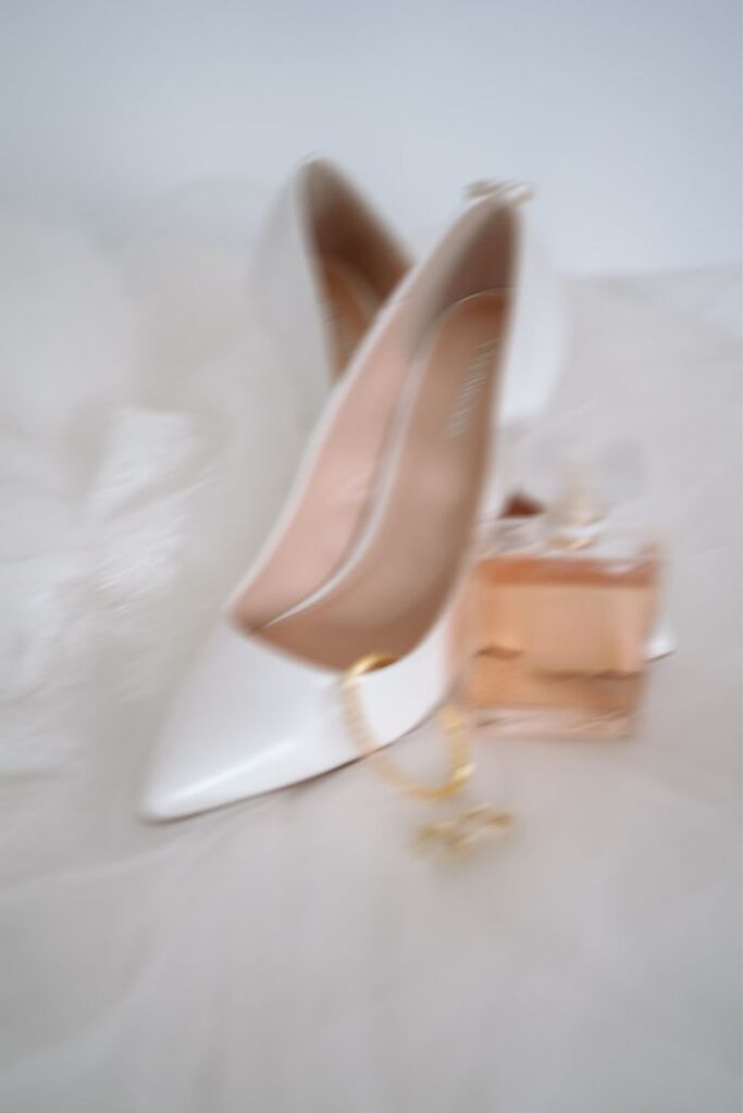 Weiße Brautschuhe mit Schmuck und Parfum als Hochzeitsdetails, verschwommen fotografiert