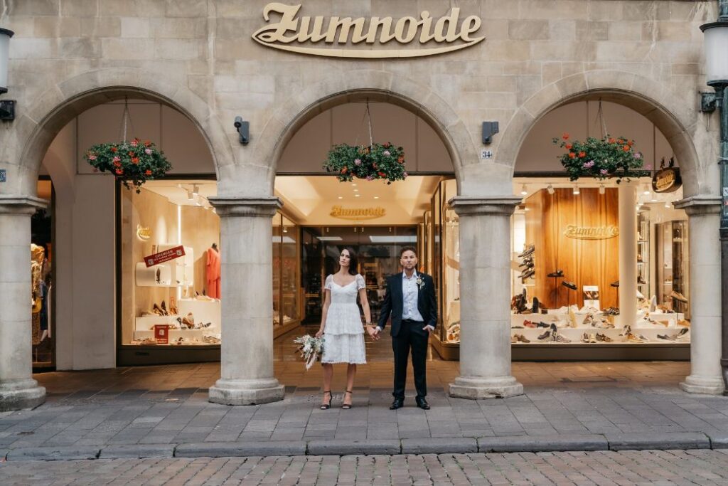 Brautpaar steht Hand in Hand vor einem Geschäft in der Innenstadt – Hochzeitsfotograf Ahaus