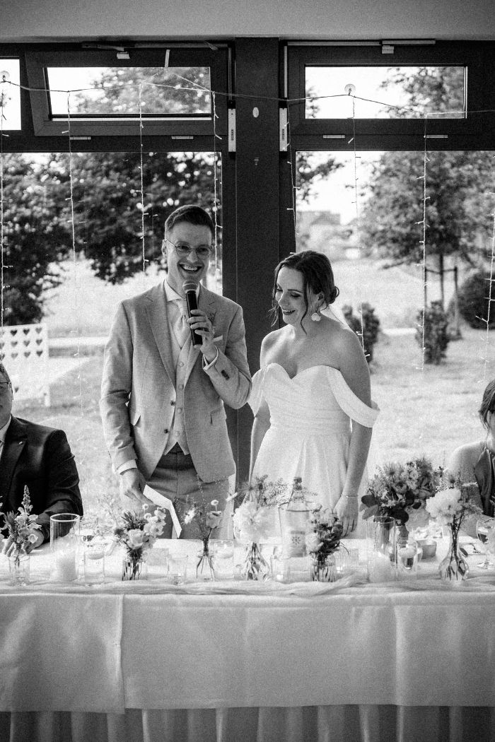 Bräutigam hält emotionale Rede neben lächelnder Braut – Hochzeitsfotograf Ahaus.