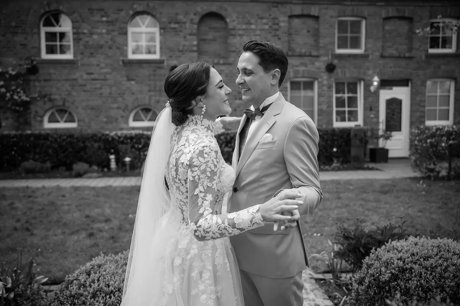 Lächelndes Brautpaar im Garten vor Backsteinhaus – Hochzeitsfotograf Ahaus