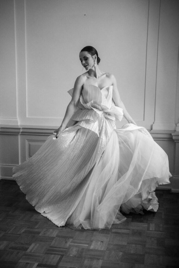 Braut im kunstvollen Hochzeitskleid dreht sich in einem eleganten Innenraum, Schwarz-Weiß fotografiert